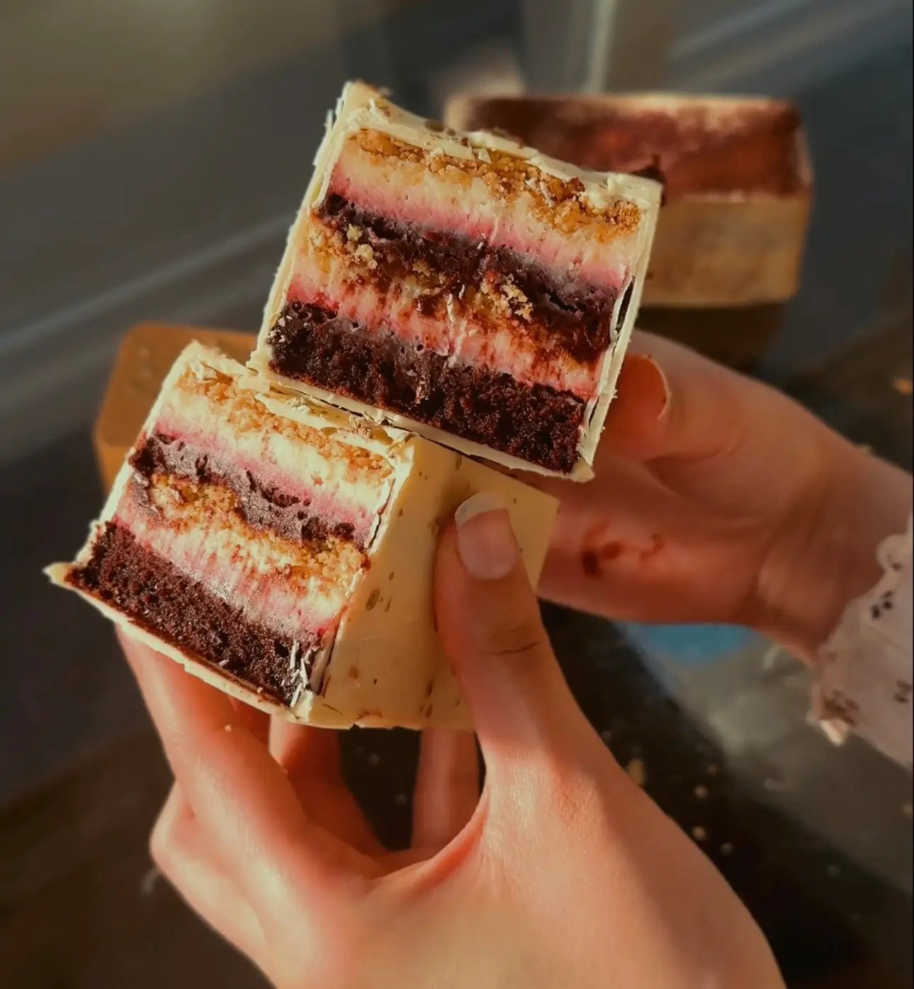 Close-up of a Red Velvet Cheesecake Patisserie Bar held by a hand with a blurred background